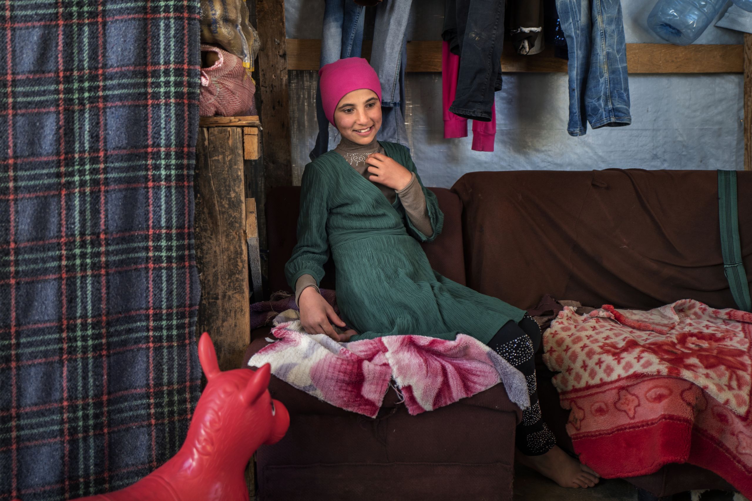 Amal sits in the semi outdoor space used by the family as living room and for storing clothes and blankets.