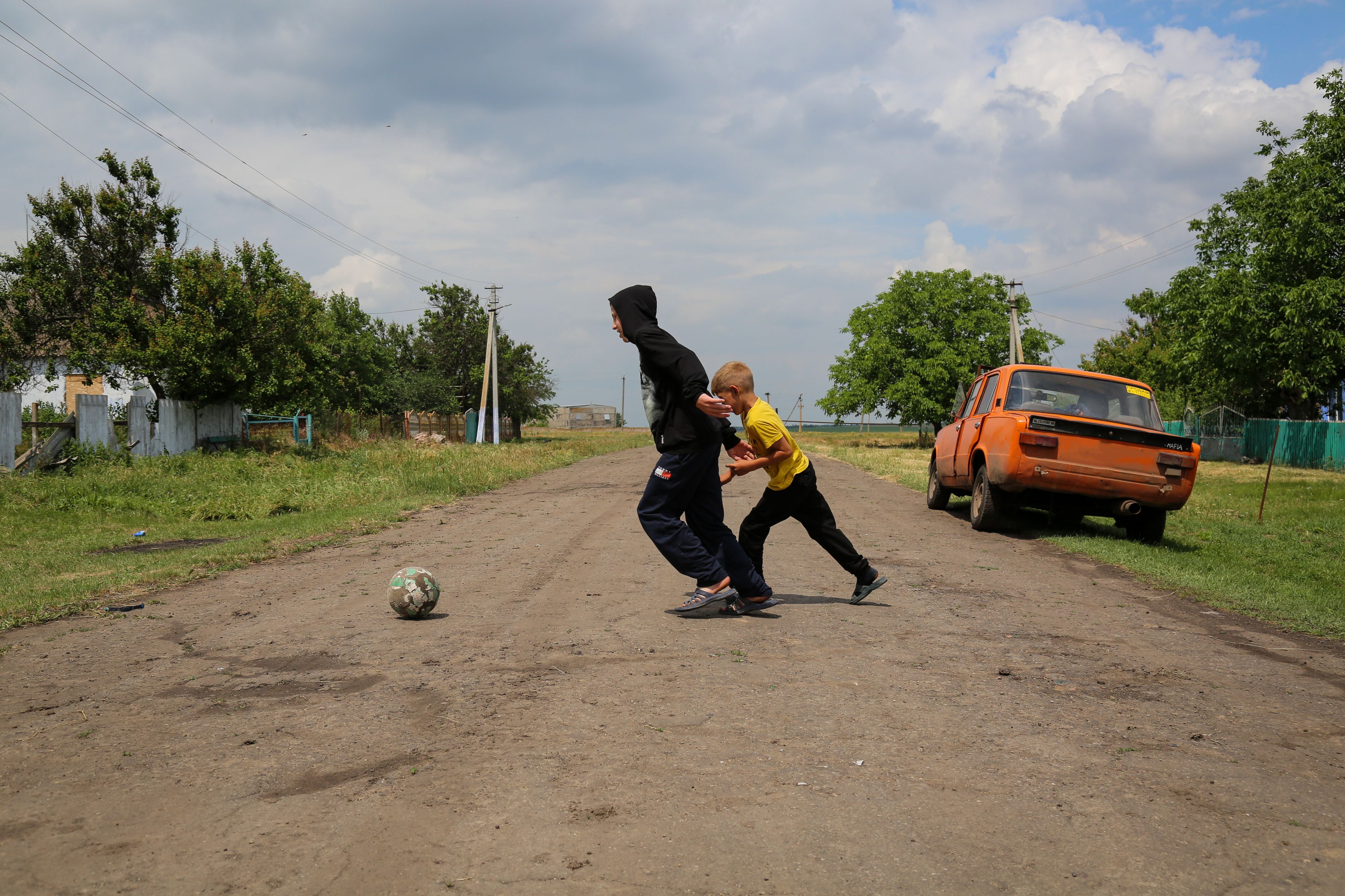 Valera*, 13, plays football with his brother Oleh*, 9 outside the family home in a village outside Mykolaiv